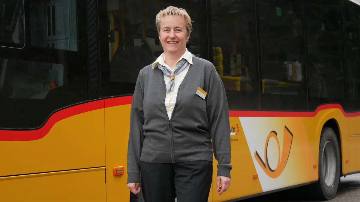 Man sieht eine Frau mittleren Alters in Dienstkleidung vor einem Linienbus.